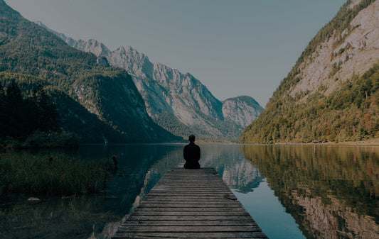 Photo of a person meditating at the end of a dock with a view of mountains